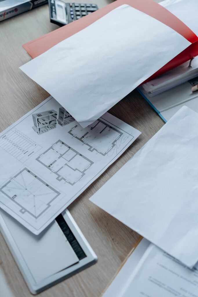 pexels-photo-8297537 High angle view of architectural floor plans and paperwork on a wooden desk in an office setting.