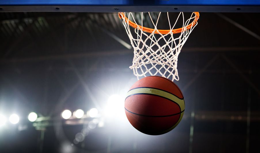 un pallone che entra nel canestro, su sfondo di palazzetto sfocato.