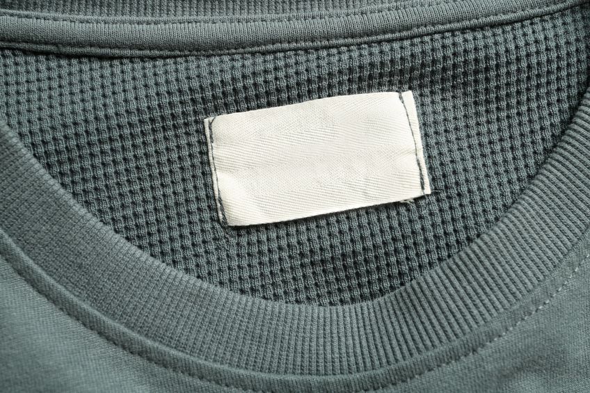 Etichetta bianca senza scritte cucita all'interno del colletto di una maglia grigia.
